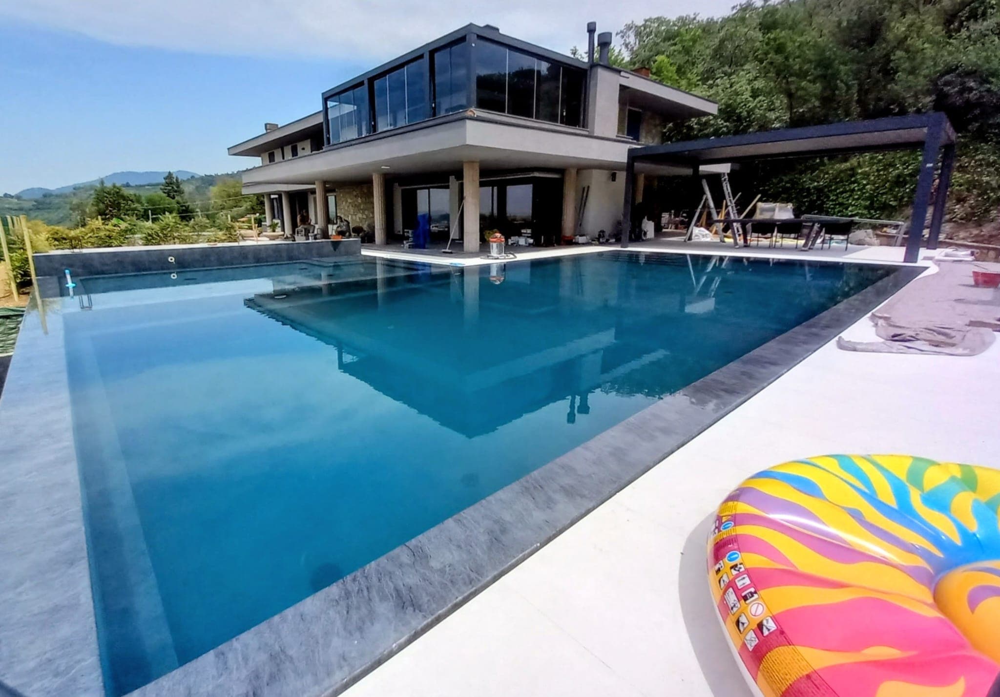 Villa moderna di lusso con grande piscina a sfioro e ciambella colorata in primo piano.